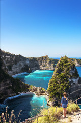 Young happy girl looking amazing view of a tropical beach, sea rocks and turquoise ocean, blue sky. Atuh beach, Nusa Penida island, Indonesia. Travel and adventure background.