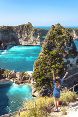 Young happy girl looking amazing view of a tropical beach, sea rocks and turquoise ocean, blue sky. Atuh beach, Nusa Penida island, Indonesia. Travel and adventure background. © olgaarkhipenko