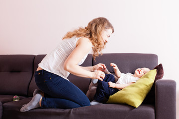 Young mother loughing tickling her adorable toddler son on their couch.