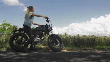 Sexy girl in casual jeans with classic style cafe racer motorcycle. Modern woman try to kick start her bike. Bike custom made in vintage garage. Brutal fun urban lifestyle. Outdoor portrait.