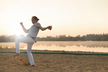 Fototapeta premium Athletic capoeira performer workout training on the beach sunris