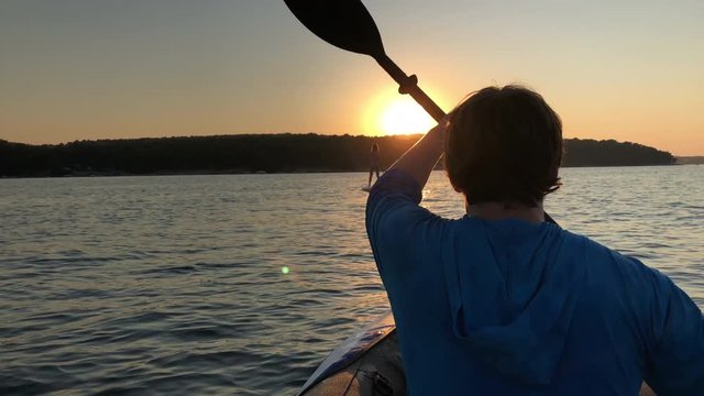 Man on kayak and woman on SUP paddling at sunset.