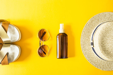 Women's summer accessories for a beach holiday with a straw hat, sunglasses and sunscreen on a yellow background. Top view, flat lay