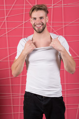 Guy bearded and attractive tearing off shirt. Man with bristle on happy face undressing, pink background. Man with beard or unshaven guy looks handsome and well groomed. Masculinity concept