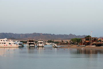 Fototapeta na wymiar Bay and ships on the water. Boat station on the shore. Low mountains in the distance. Red sea coast, Egypt