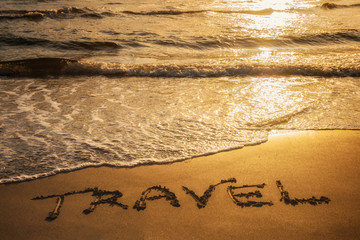 Travel text written in the sand during sunset over the ocean. Travel concept.