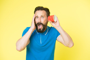 Shocking rumors. Man bearded mature guy eavesdrops with cup yellow background. Find out new scandalous rumors first. Guy shocked eavesdrops scandalous rumors. Curiosity and impoliteness