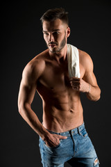 Fototapeta premium Undress for you. Athlete with sexy muscular body on confident face. Man muscular torso tense muscles veins hand in pocket denim pants. Macho muscular chest looks attractive black background