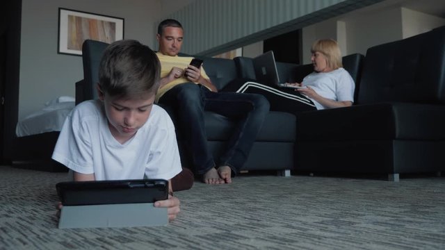 Happy family mom, dad and son watching movies and playing games on phones and laptops