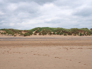 grassy sand dunes at the edge of a flat sandy beach with footprints in summer sunlight with blue sky and clouds on the west coast of lancashire england