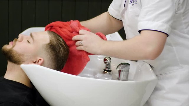Preparing for the haircut. Male barber washing the head of the young man in barber's. 4K
