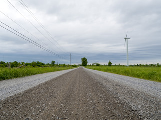 Fototapeta na wymiar Straight gravel road landscape with a wind turbine and power lines 