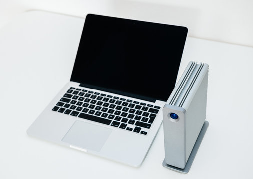 External HDD hard disk drive next to modern powerful new aluminum laptop on white table - focus on the HDD disk drive