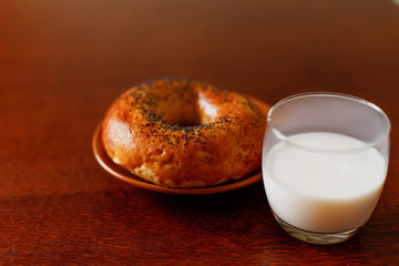 A glass of fresh milk and a delicious bagel with poppy on a wooden table. Healthy food.