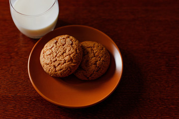 A glass of fresh milk and oatmeal cookies on a wooden table.