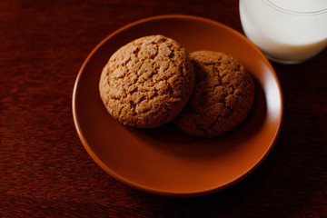 A glass of fresh milk and oatmeal cookies on a wooden table.