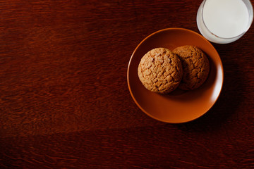 A glass of fresh milk and oatmeal cookies on a wooden table.