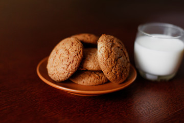 A glass of fresh milk and oatmeal cookies on a wooden table.