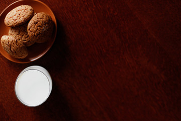A glass of fresh milk and oatmeal cookies on a wooden table.