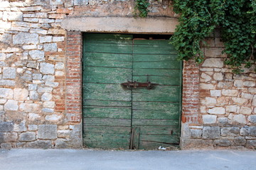 Old green wooden garage doors with heavy metal lock and brick frame inside traditional stone wall