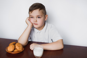 Boy is sitting with a cookie and milk at the table and waiting.