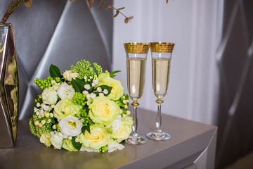 Two glasses of champagne and wedding bouquet of white roses on table