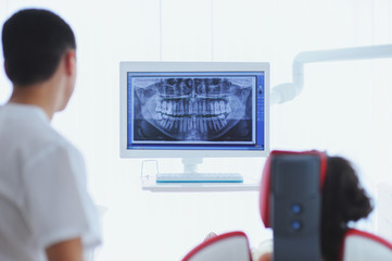 A dentist shows the young patient an X-ray of the teeth on the monitor display in the dental office.