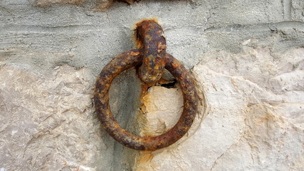 Large completely rusted metal hook with strong ring mounted on traditional stone and concrete wall used for tying up boats