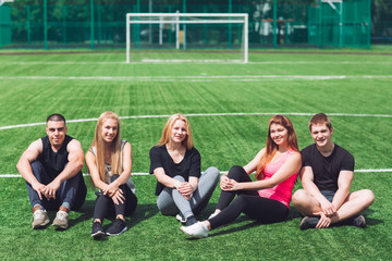 Young people sit on the grass on the football field.