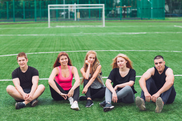Young people sit on the grass on the football field.