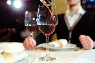Waiter pouring red wine in a glass at a restaurant table