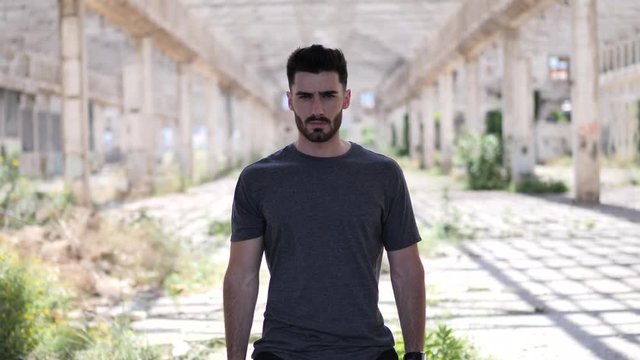 Handsome young man in empty warehouse, looking at camera and crossing arms on his chest