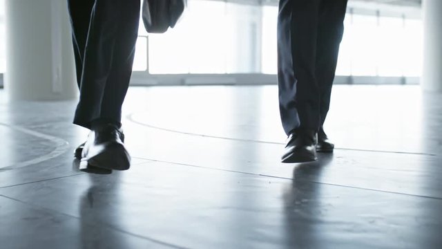 Closeup low angle shot of legs of two unrecognizable businessmen walking towards the camera in hall of office building