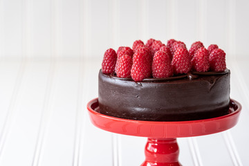 Chocolate cake with red raspberries on top, on a red cake platter, against a white background
