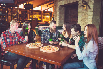 Friends having a drinks in a bar, They are sitting at a wooden table with beers and pizza.