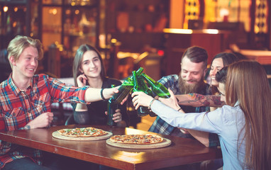 Friends having a drinks in a bar, They are sitting at a wooden table with beers and pizza.