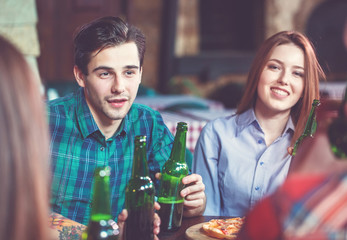 Friends having a drinks in a bar, They are sitting at a wooden table with beers and pizza.