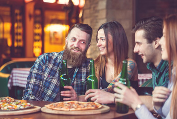 Friends having a drinks in a bar, They are sitting at a wooden table with beers and pizza.