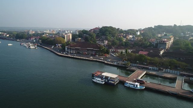 Aerial view on the left bank of the Mandovi river and Panjim city, Goa, India. Road traffic on the street along the riverbank. Shooting with a drone.