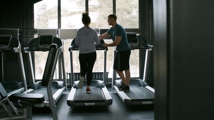 Rear view of sportswoman exercising on treadmill in empty gym under guidance of young male coach