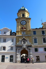 Antique clock tower building situated on main square with old building around it and blue summer...