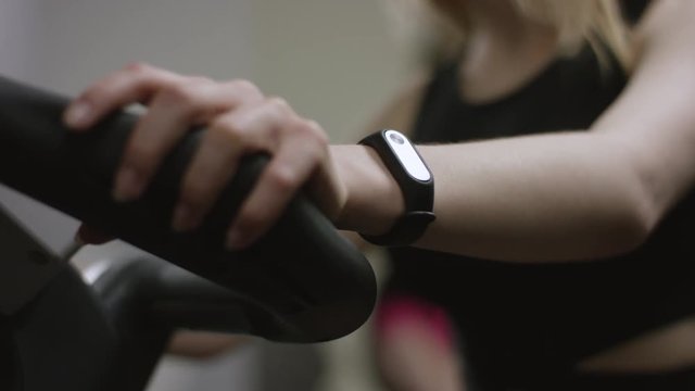 beautiful girl in black sport wear hardly working on exercise bike and watching for her puls with focus on hands in the new gym