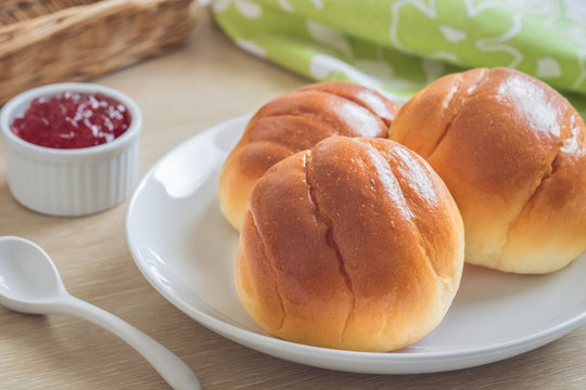 Round bun, bread rolls on white plate and strawberry jam