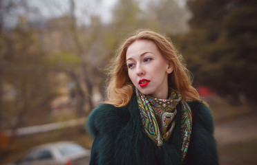 Naklejka premium Red-haired girl in autumn park. She's wearing short coat and scarf. Close-up portrait. Female lips with red lipstick. Romantic mood.
