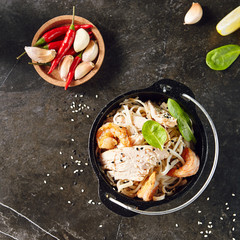 Noodles with Shrimps, Chicken, in Metal Bowler with Sesame Seeds on Natural Dark Stone Background