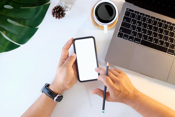 Man's hand holding white mobile phone  on desk in office