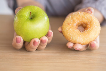 woman hands holding green apple and donut  ,healthy or unhealthy eating concept 