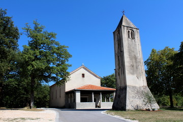 Naklejka premium Stone bell tower with old renovated church in background surrounded with trees and paved road