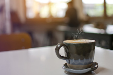 Cup of steaming hot coffee on the wooden table with blurred man sitting in the cafe