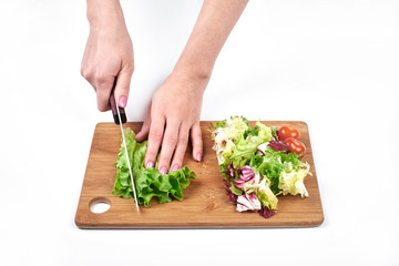 Closeup of woman hands slicing salad and vegetables on a wooden board, isolated on white background, copy space